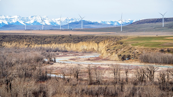 A wide river valley with wind turbines and snow-capped mountains in the background